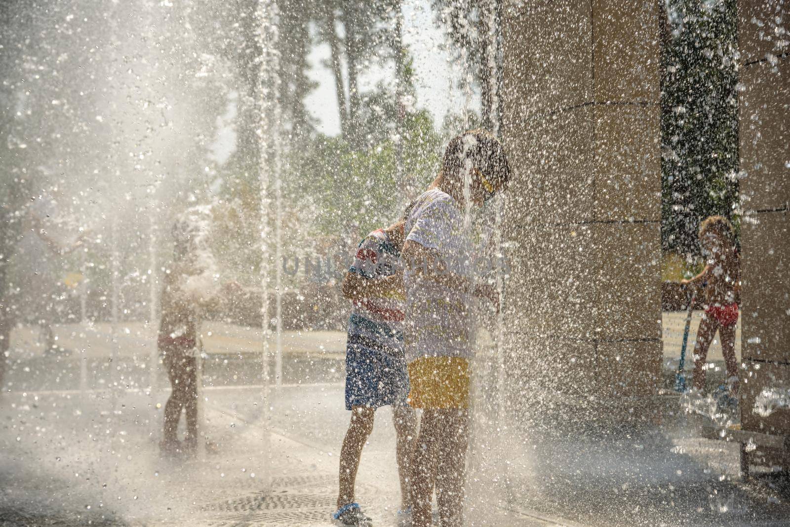 Boy having fun in water fountains. Child playing with a city fountain on hot summer day. Happy kids having fun in fountain. Summer weather. Active leisure, lifestyle and vacation.