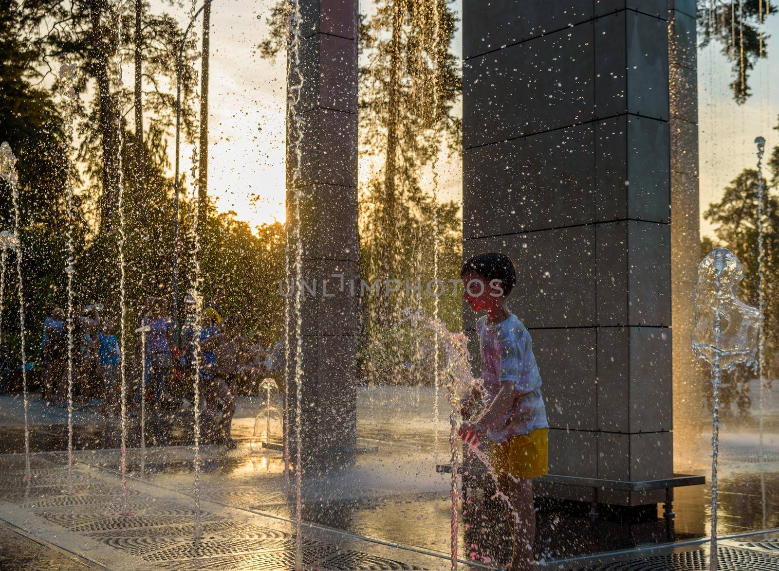 Boy having fun in water fountains. Child playing with a city fountain on hot summer day. Happy kids having fun in fountain. Summer weather. Active leisure, lifestyle and vacation.