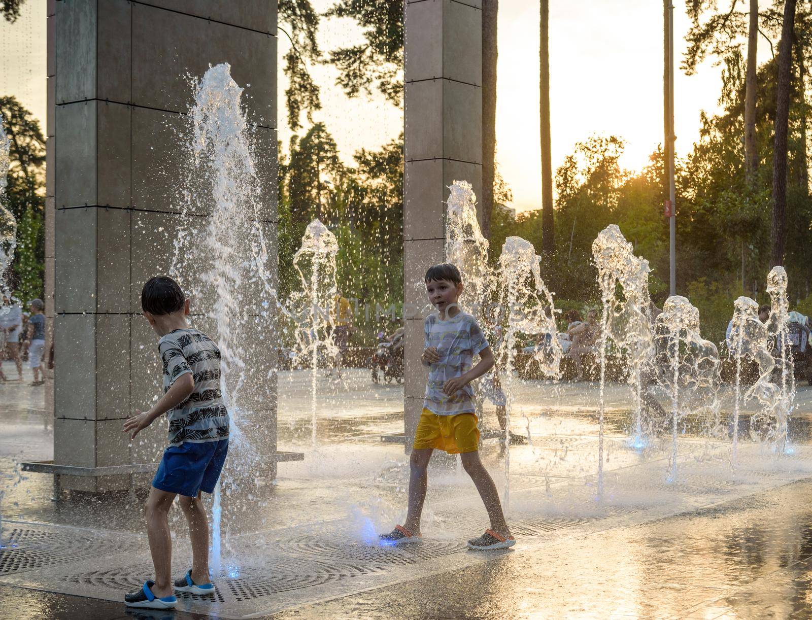 Boys jumping in water fountains. Children playing with a city fountain on hot summer day. Happy friends having fun in fountain. Summer weather. Friendship, lifestyle and vacation.