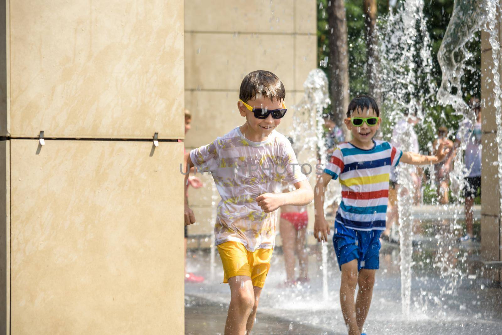 Boy having fun in water fountains. Child playing with a city fountain on hot summer day. Happy kids having fun in fountain. Summer weather. Active leisure, lifestyle and vacation.