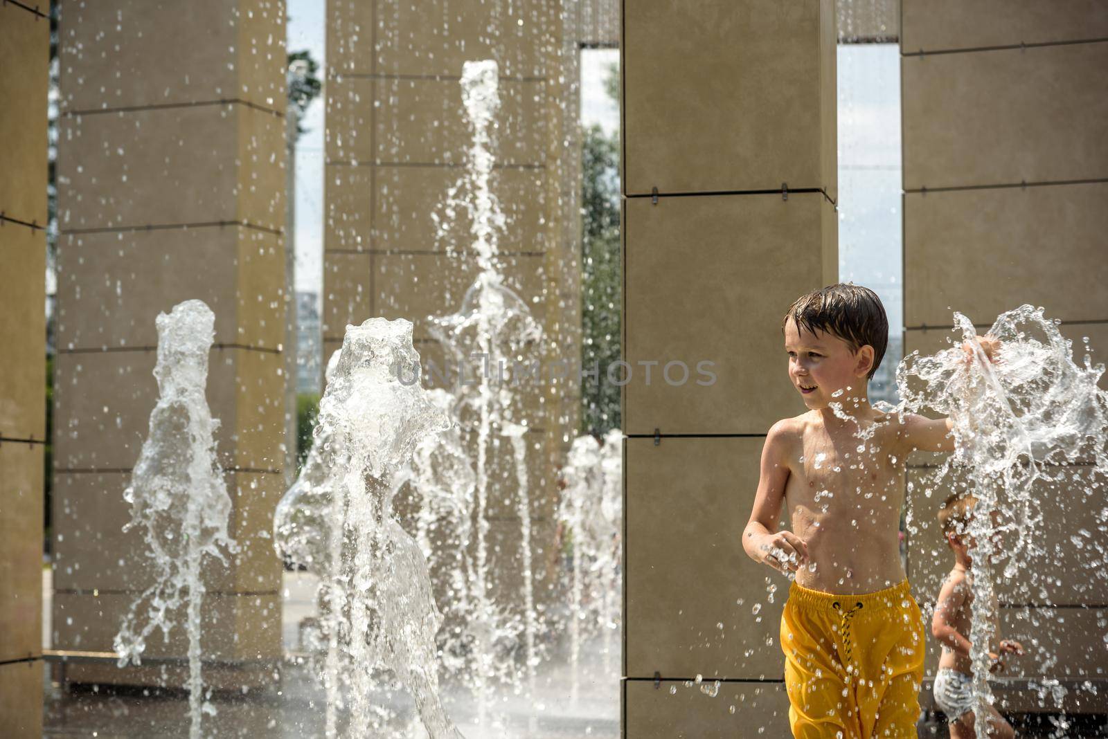 Boy having fun in water fountains. Child playing with a city fountain on hot summer day. Happy kids having fun in fountain. Summer weather. Active leisure, lifestyle and vacation.