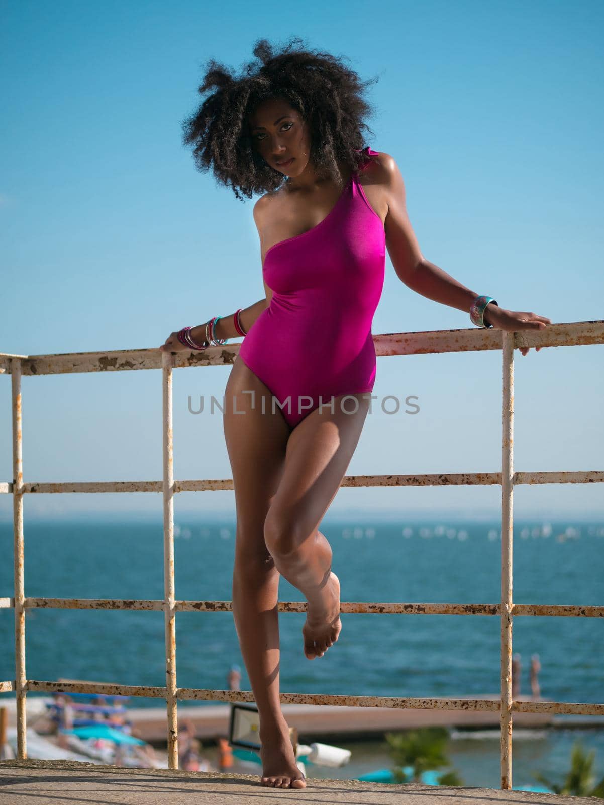 Portrait of cheerful black people, pretty happy young afro american woman smiling on sea beach. Sexy girl in pink swimsuit and jewelry enjoying nature.Lady wearing bikini. by kristina_kokhanova