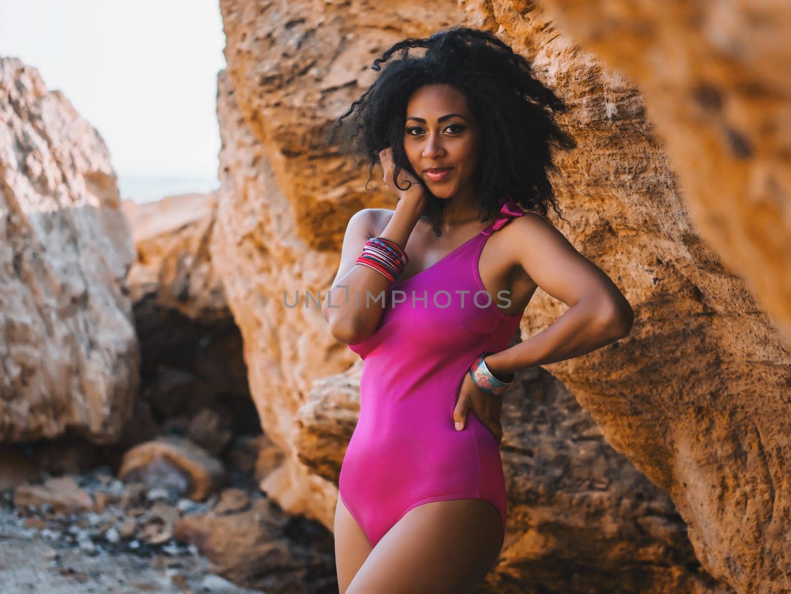Portrait of black people, pretty happy young african american woman smiling. Rocks beach. Sexy girl in pink swimsuit and jewelry enjoying nature. Travel, holiday concept.