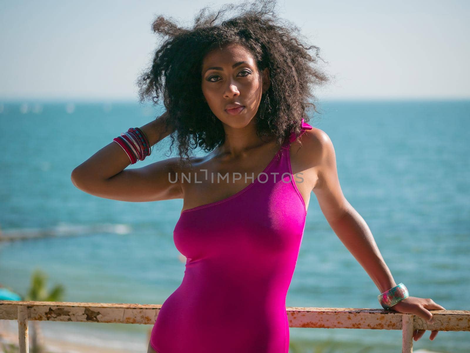 Portrait of cheerful black people, pretty happy young afro american woman smiling on sea beach. Sexy girl in pink swimsuit and jewelry enjoying nature.Lady wearing bikini.