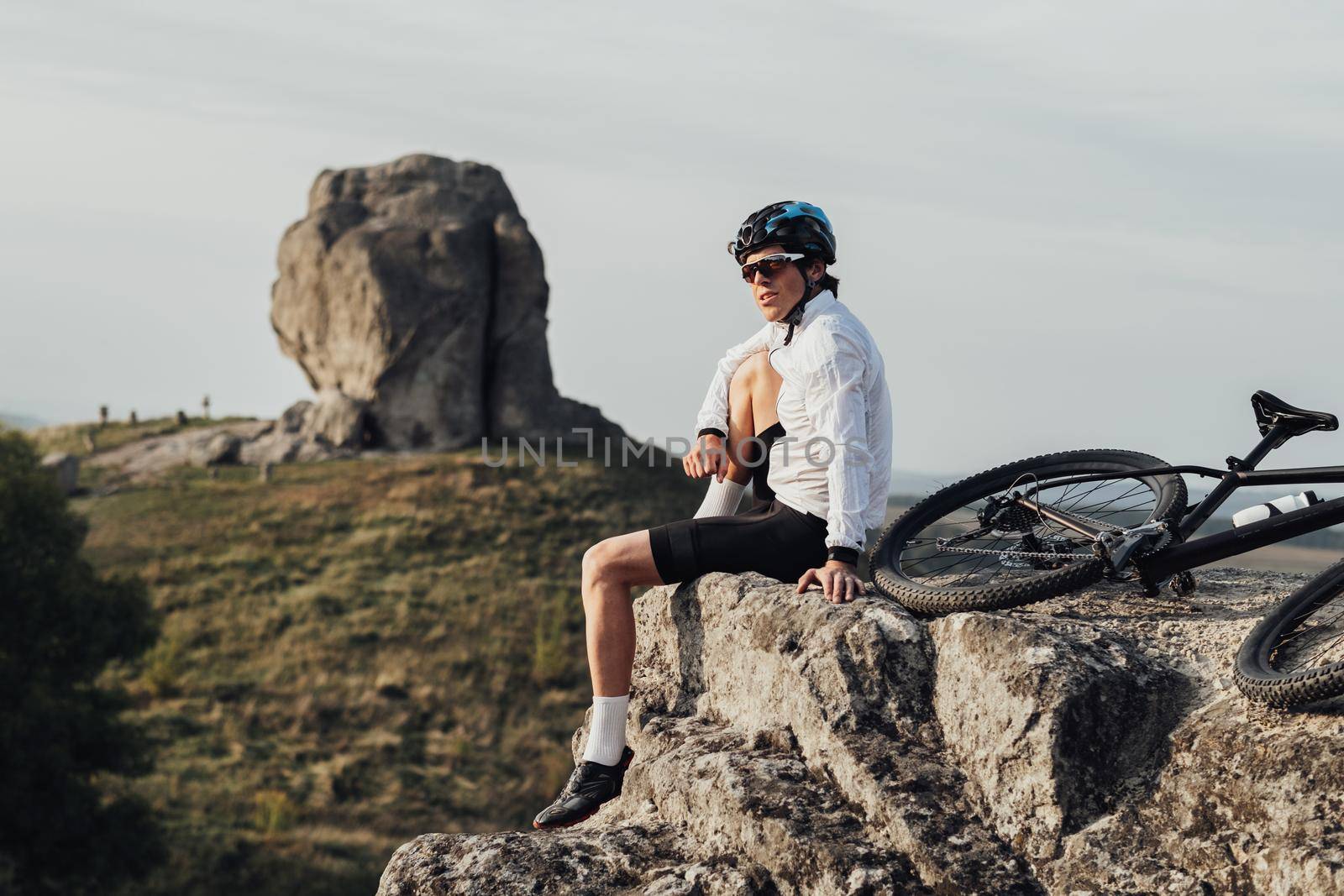 Equipped Professional Male Cyclist Sitting with Mountain Bike on Edge of the Rock and Enjoys Panoramic View on Giant Stone, Miracle of Nature by Romvy