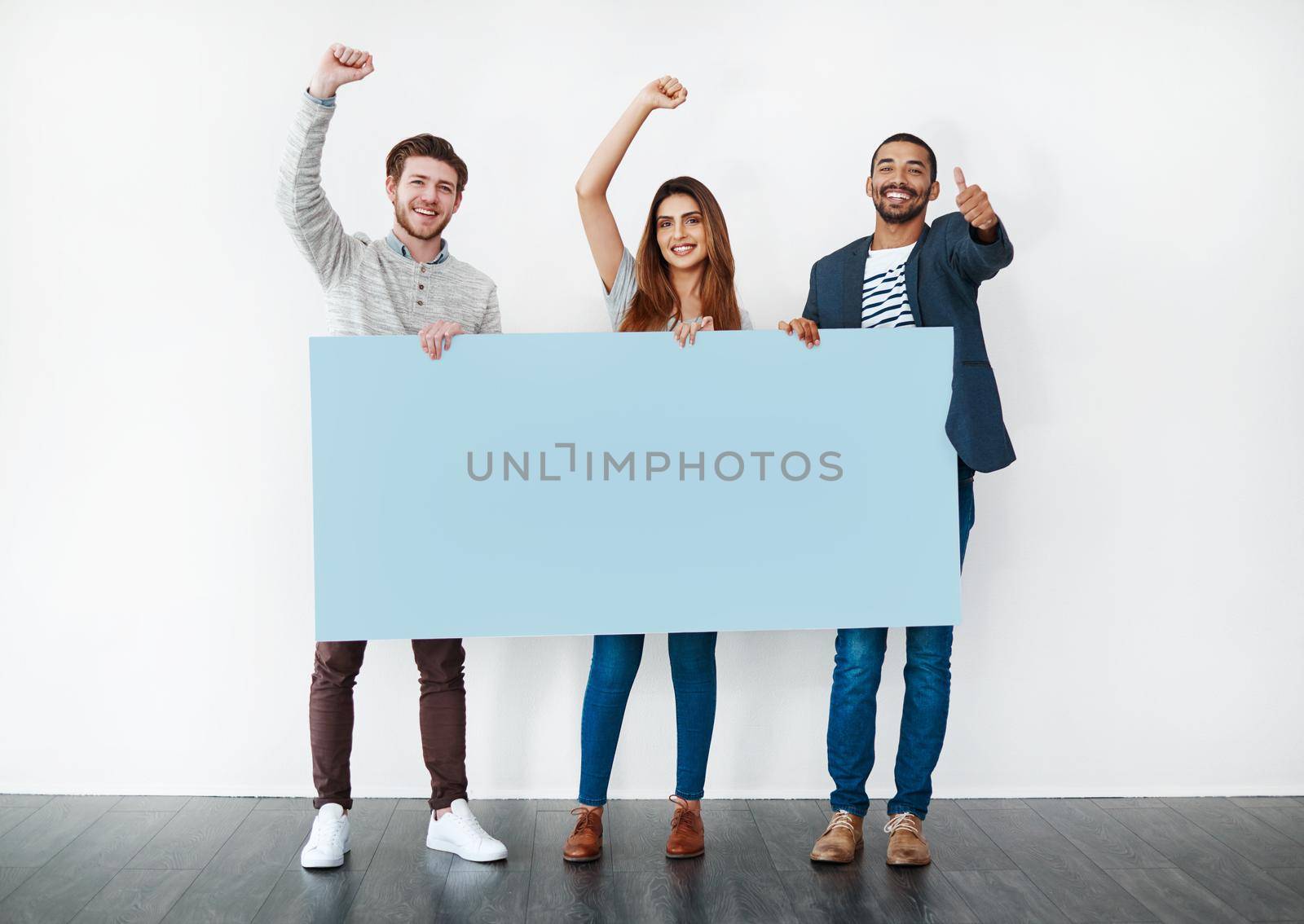 We absolutely love it. Studio shot of a diverse group of young people holding a blank placard and cheering against a white background. by YuriArcurs