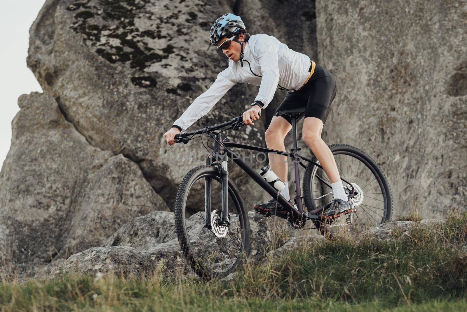 Equipped Professional Cyclist Descends a Slope on His Mountain Bike, Sportsman Going Down from Hill on Bicycle, Giant Stone on Background