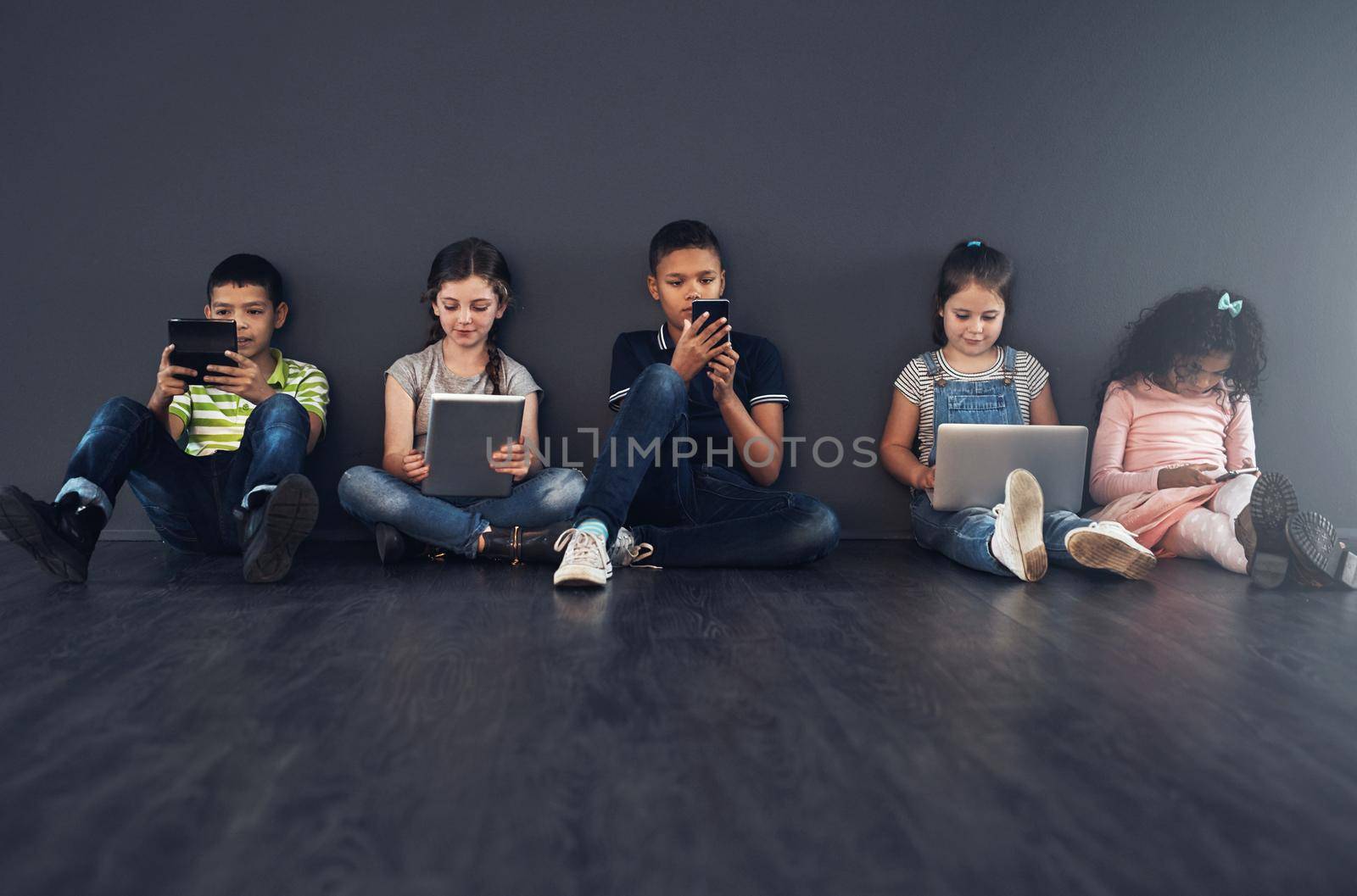 Learning to be technology literate. Studio shot of kids sitting on the floor and using wireless technology against a gray background