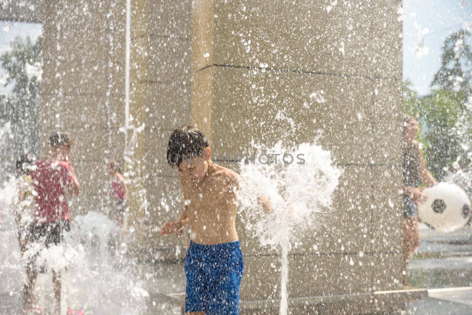 Boy having fun in water fountains. Child playing with a city fountain on hot summer day. Happy kids having fun in fountain. Summer weather. Active leisure, lifestyle and vacation.