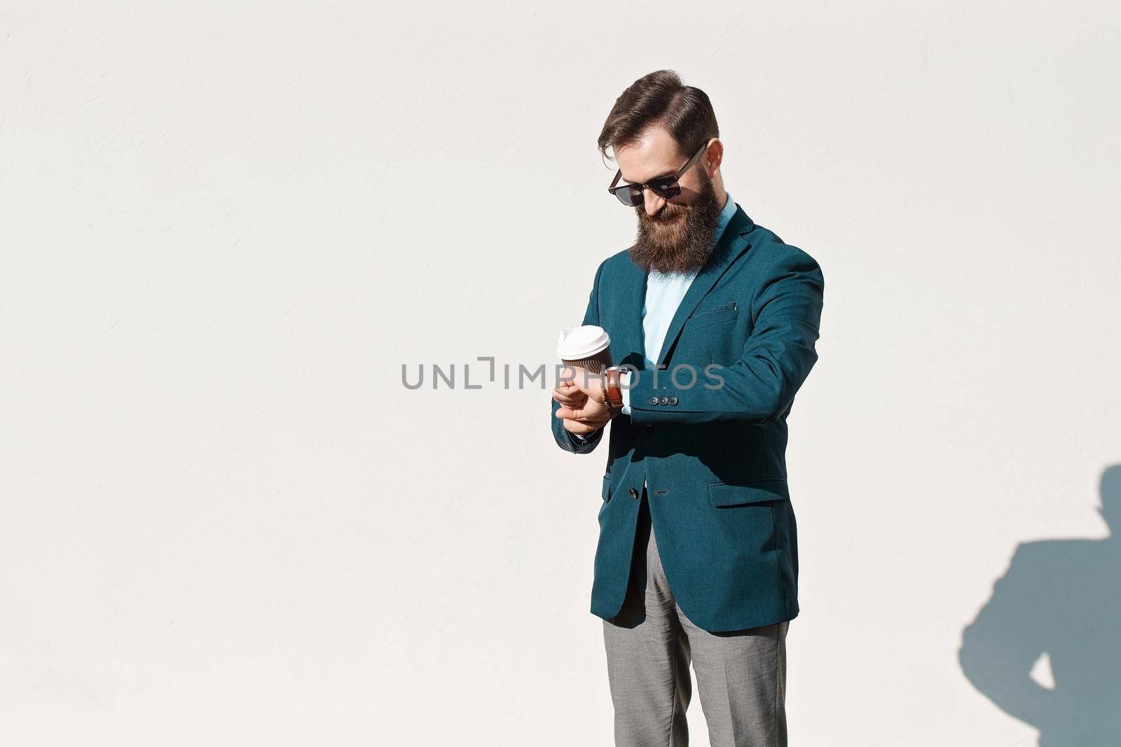 Stylish man with beard wearing a jacket, shirt and bow tie cheking time