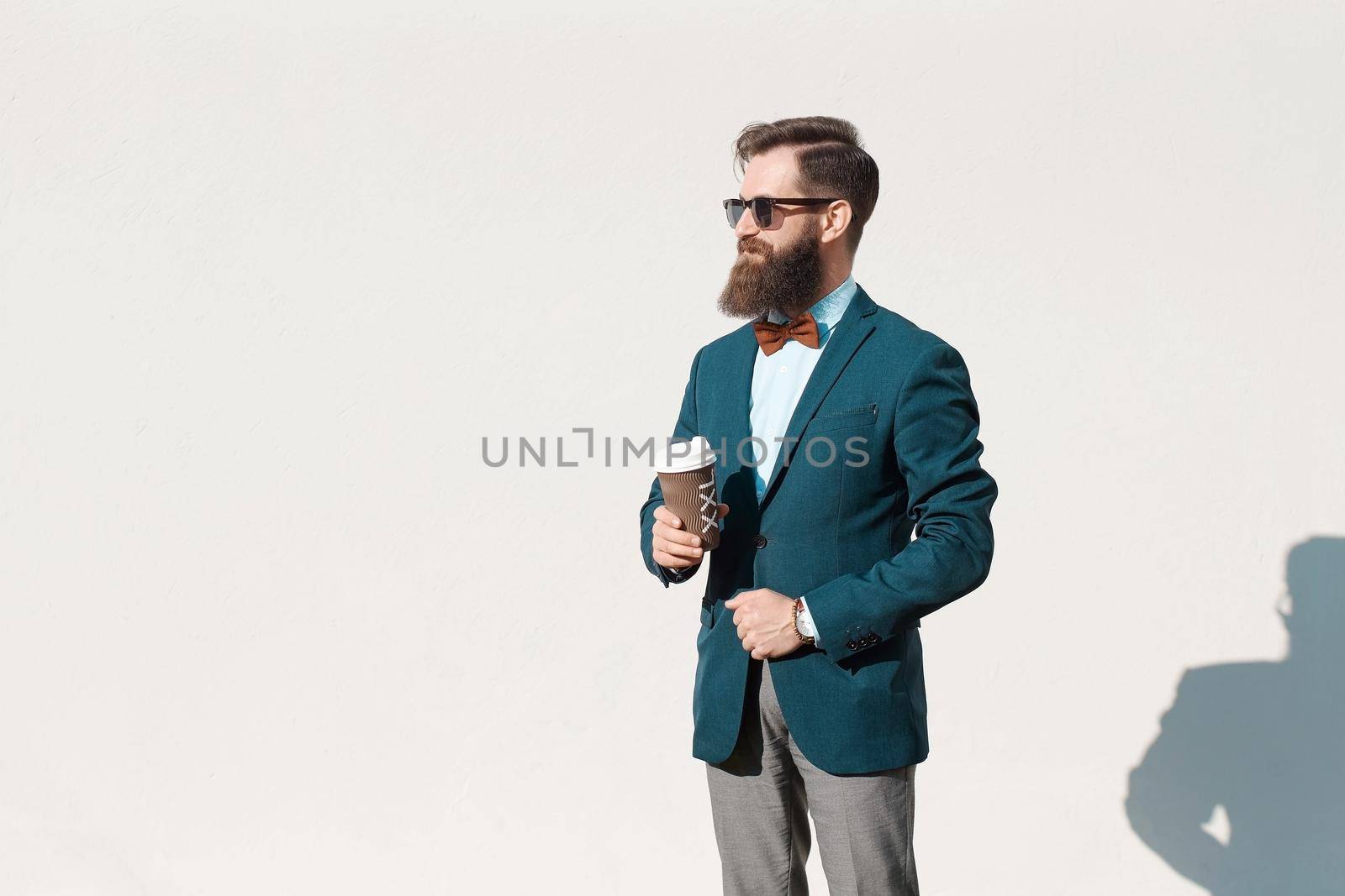 Stylish man with beard wearing a jacket, shirt and bow tie holding a coffee