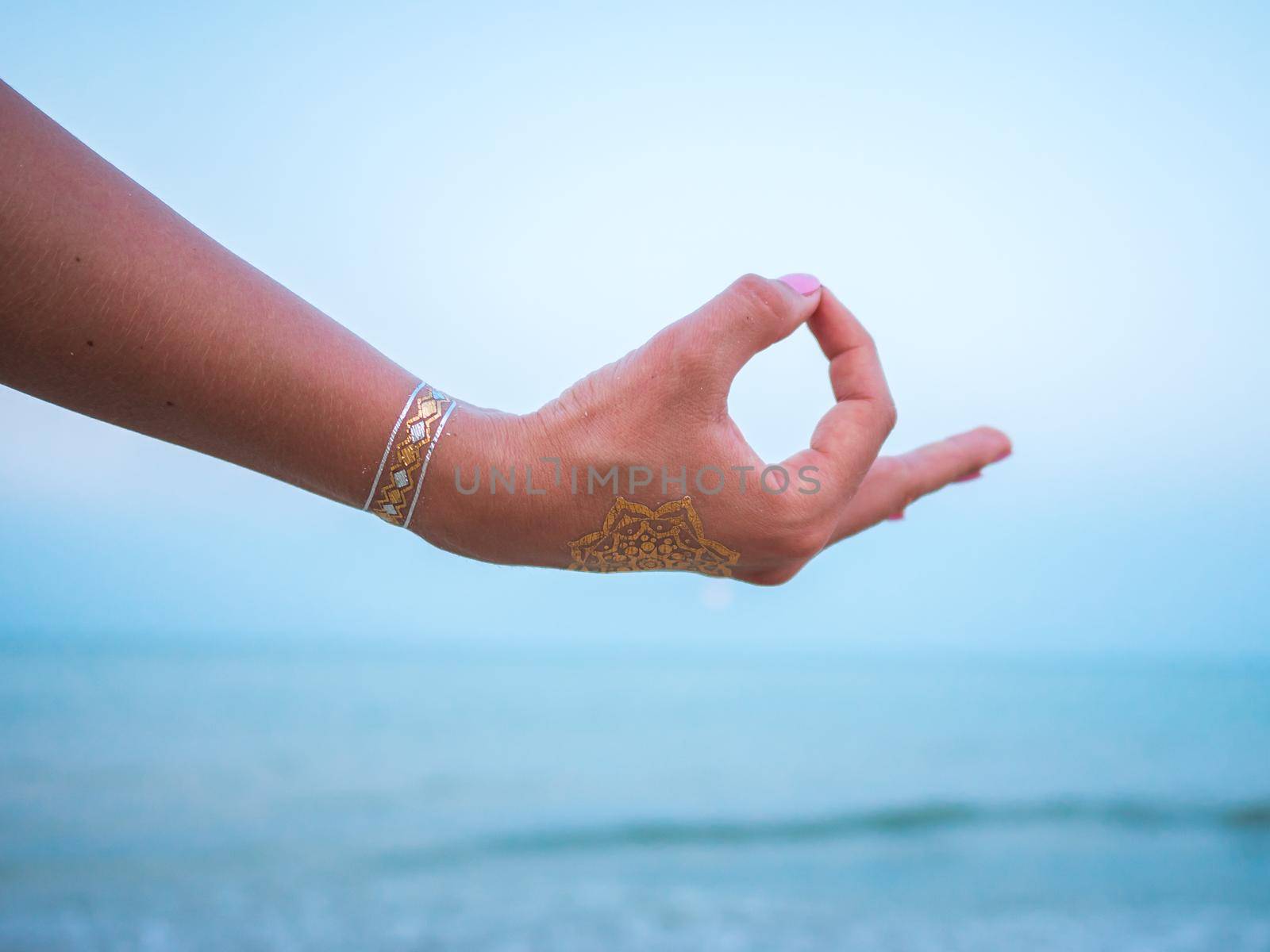 Silver and golden flash tattoo on female hands over sea or ocean background. Woman practicing yoga. Gyan Mudra. by kristina_kokhanova