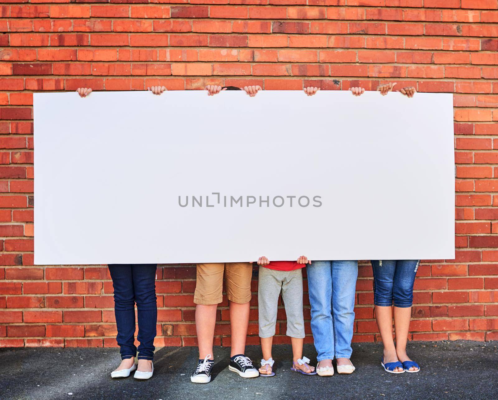 Weve saved this space for you. a group of young children holding a blank sign against a brick wall. by YuriArcurs