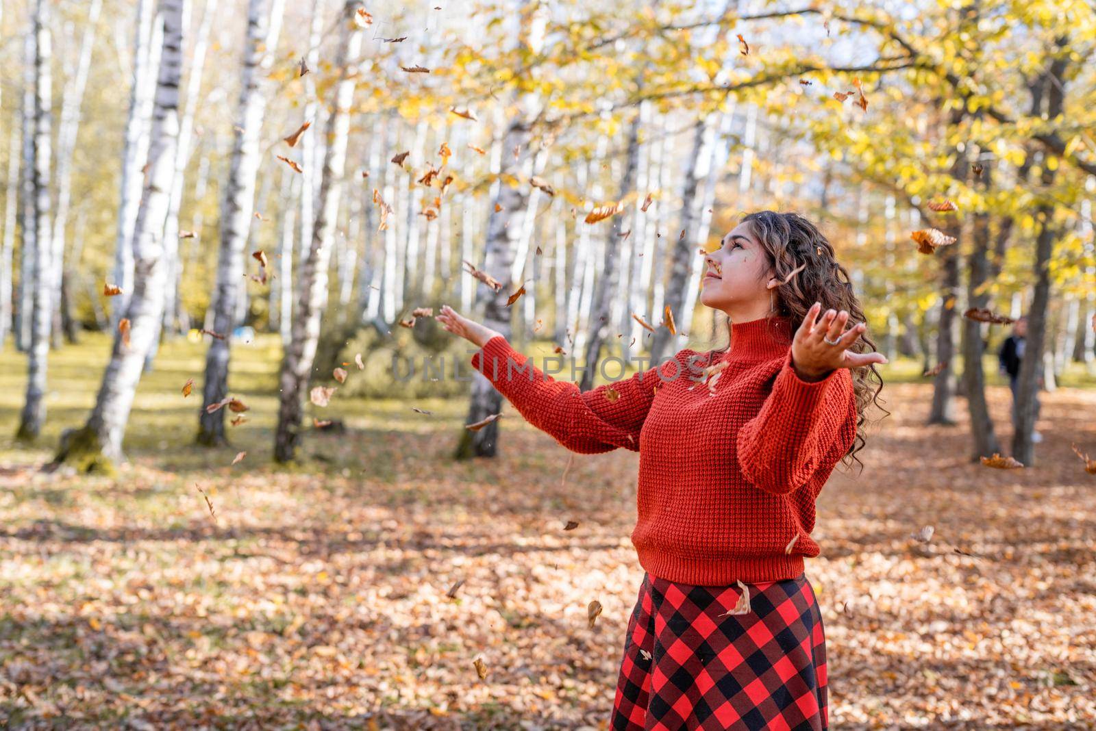 Autumn nature. Young happy woman in red sweater throwing leaves in autumn forest