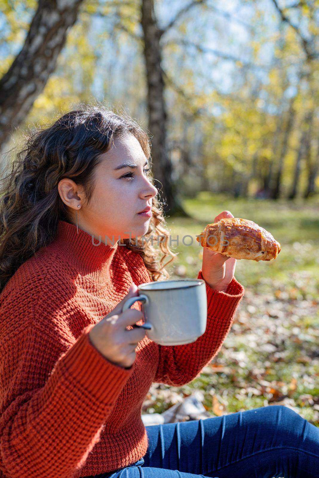 Leisure, free time. Beautiful caucasian woman in red sweater on a picnic outdoors, sitting on a plaid in autumn forest
