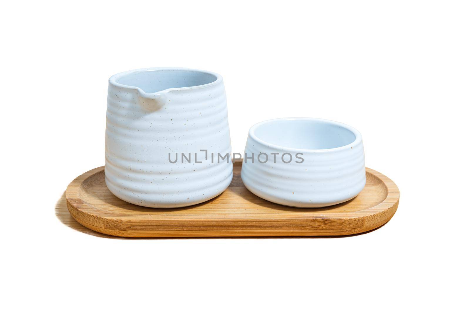 A set of ceramic mug and jug of tea, made of white clay, on a wooden plate on white background.