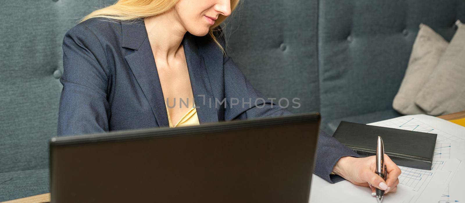 Young businesswoman sitting at the table and writing in a notebook. Adult woman working with papers at the cafe