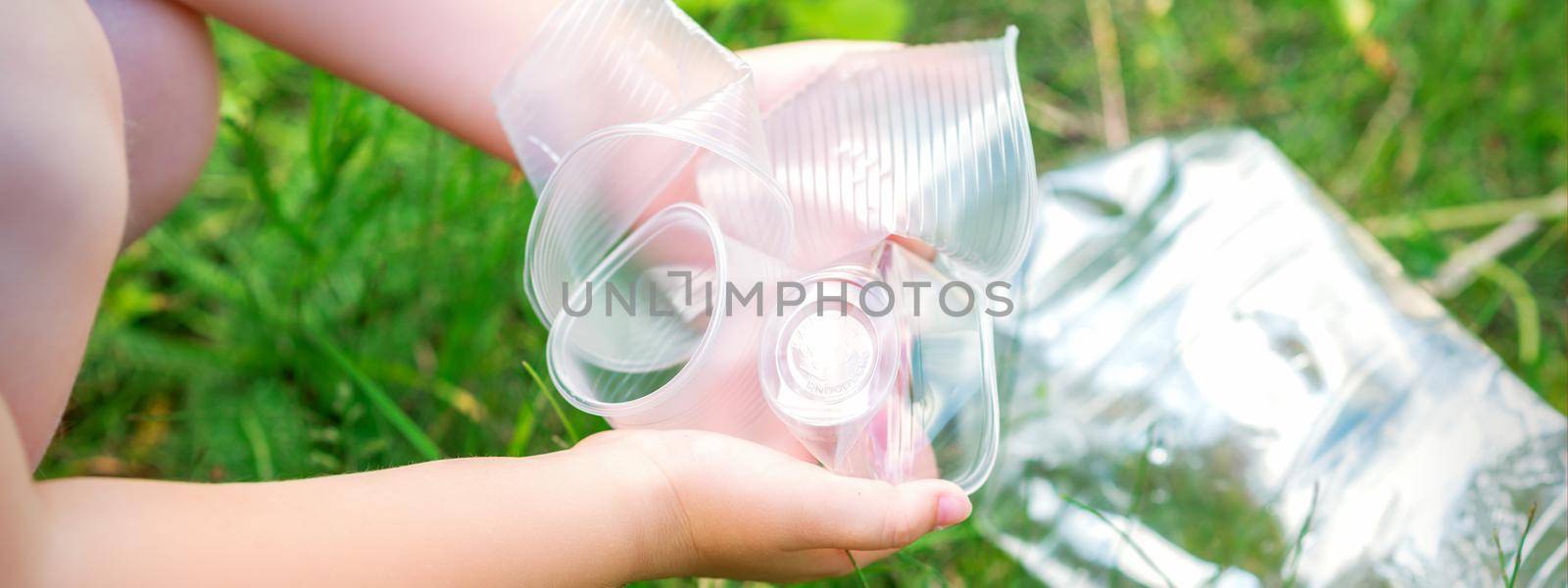 Child's hands clean the park from used plastic utensils in the grass