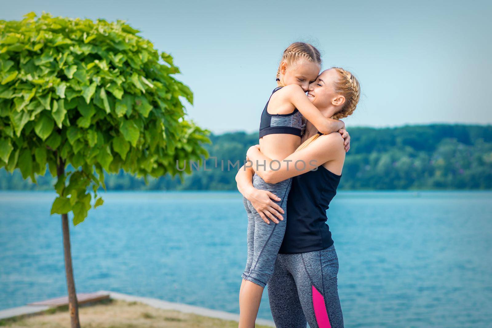 Mother embracing her daughter near the pond wearing sportswear outdoors