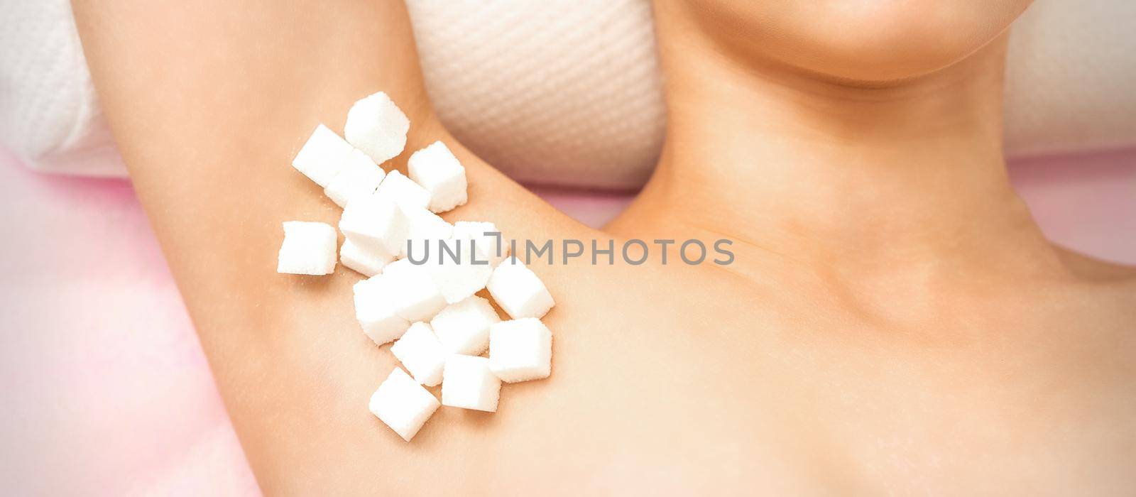 Sugaring concept. White sugar cubes lying on the armpit of a young female