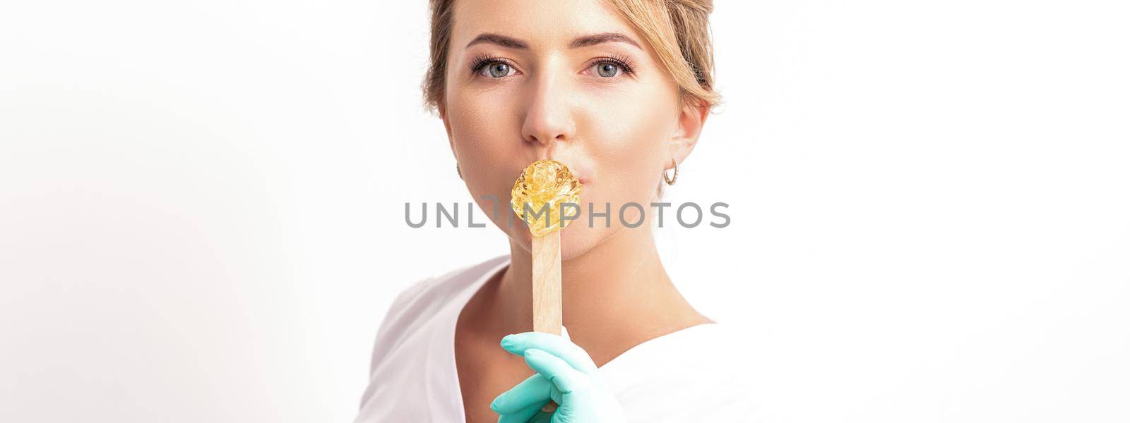 Portrait of female cosmetologist holds a wooden stick with a wax covering her lips on white background