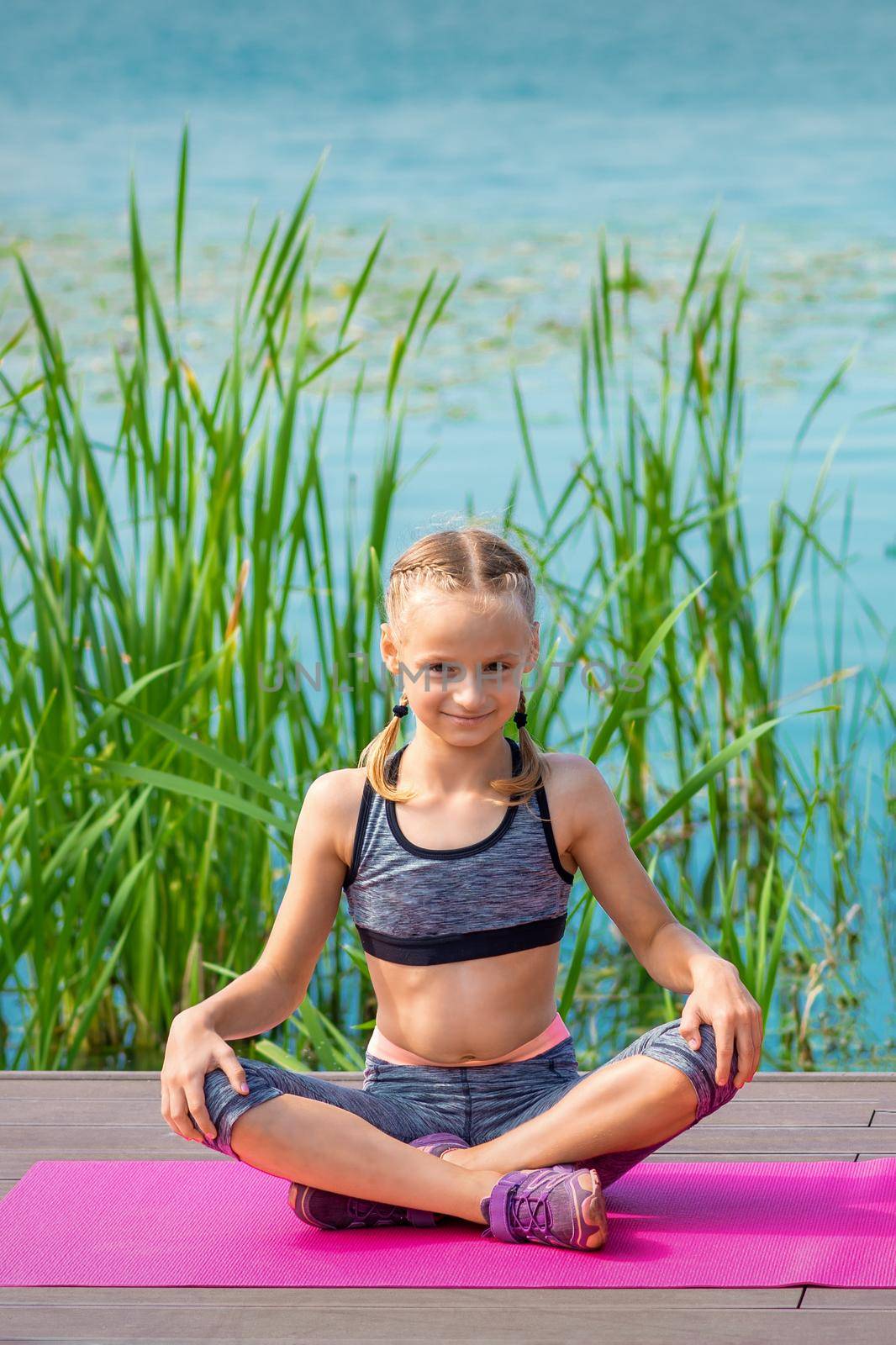 Child in sportswear sitting on the mat on the pier near the water outdoor
