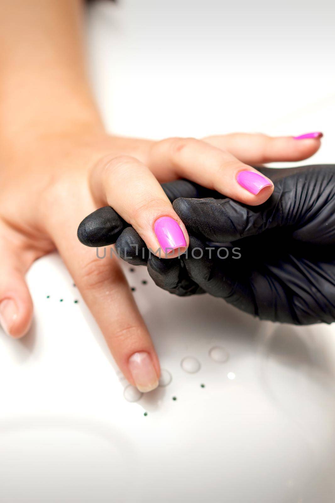 Manicure master's hand holds a female finger with purple nail polish while painting the nails in a nail salon