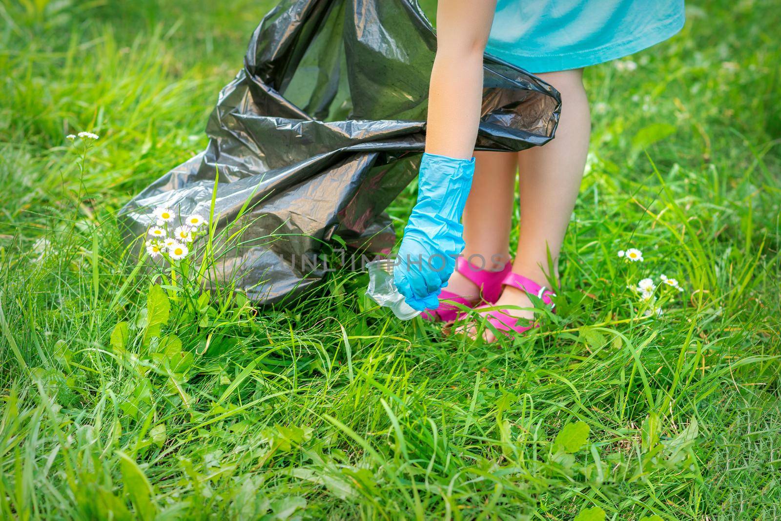 Child's hand cleans park from plastic utensils in the grass in the park