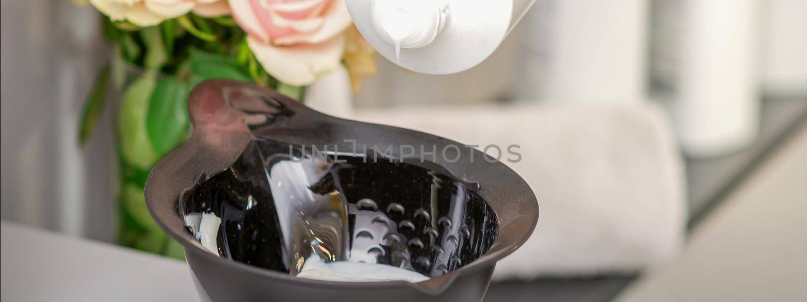 Hairdresser's hand mix hair dye in a black bowl in a beauty salon
