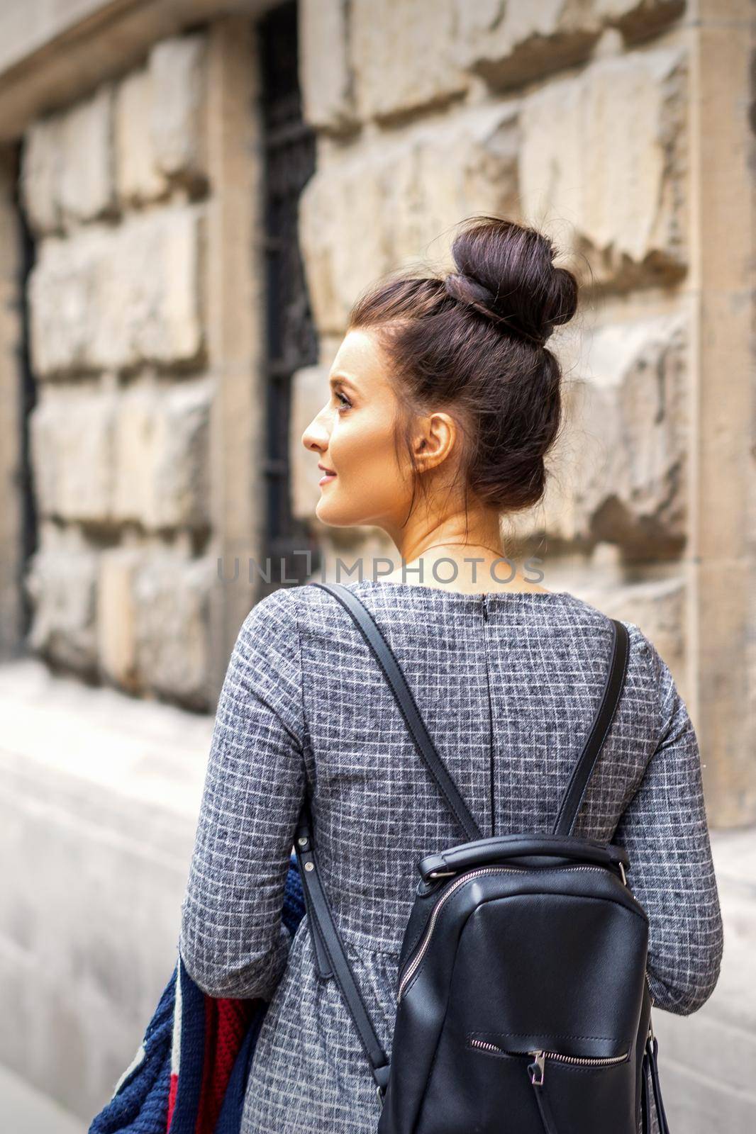 Back view of a young woman with a backpack walks in a European city