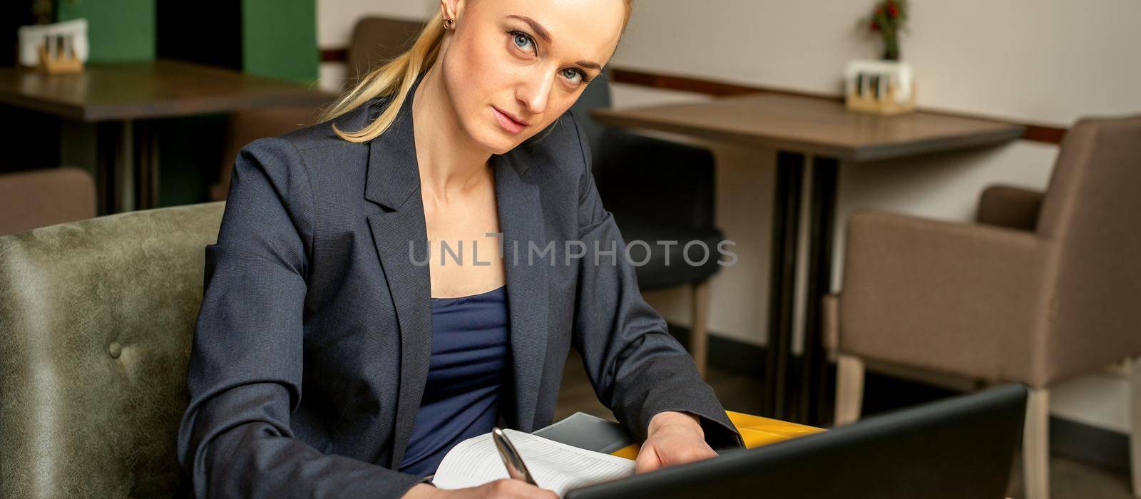 Portrait of a young caucasian businesswoman with pen and laptop at the table looking at the camera in a cafe
