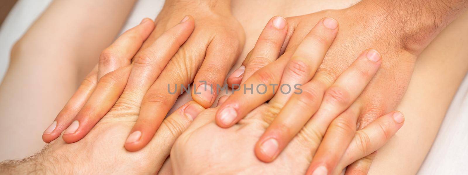 4 hands massage the patient back. Two masseurs doing massage. Closeup