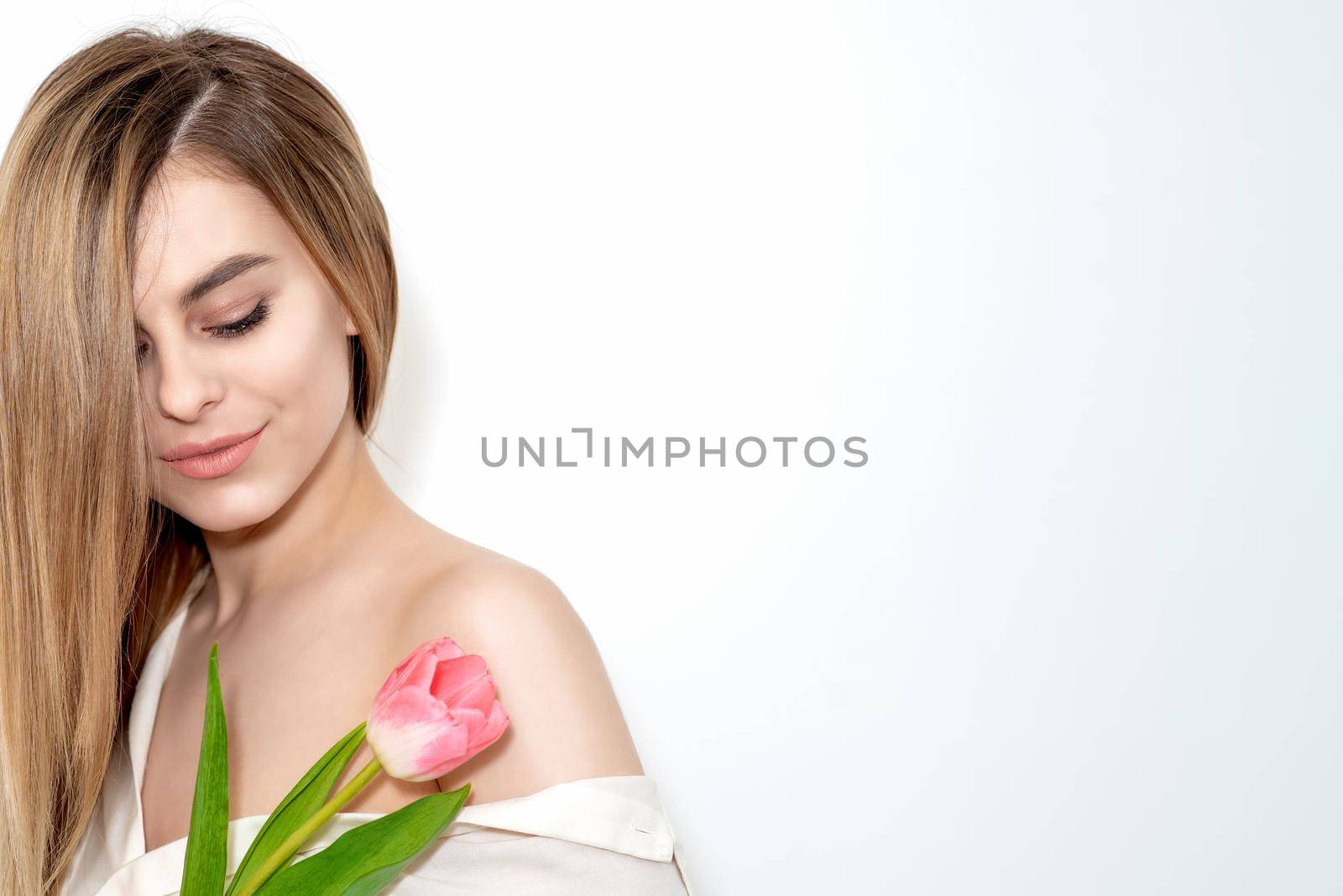 A portrait of a happy young caucasian woman with closed eyes and one pink tulip against a white background with copy space