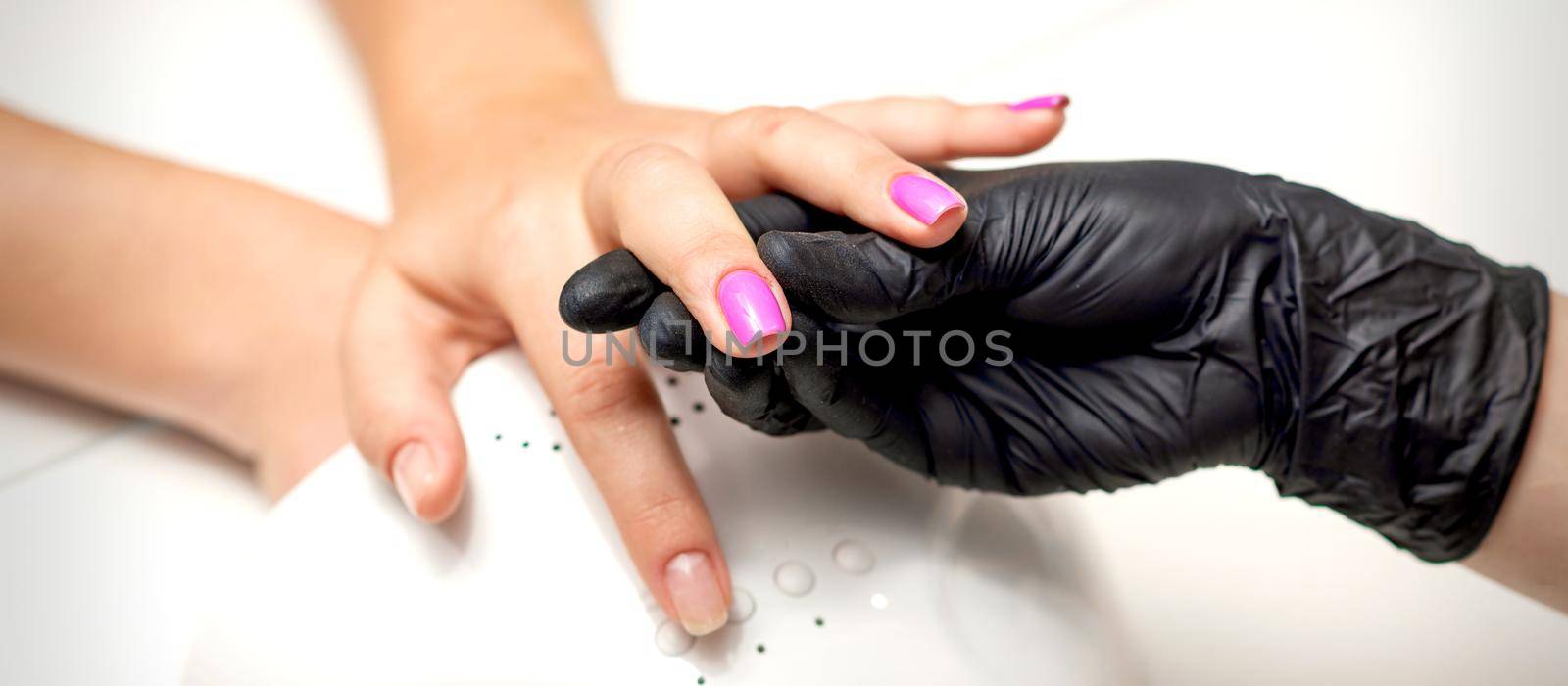 Manicure master's hand holds a female finger with purple nail polish while painting the nails in a nail salon