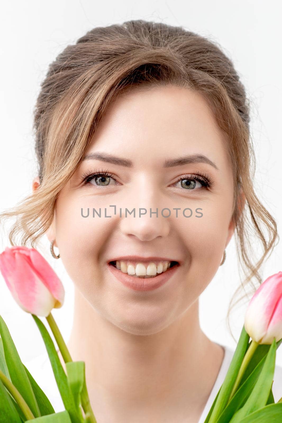 Portrait of a happy young caucasian woman with pink tulips against a white background