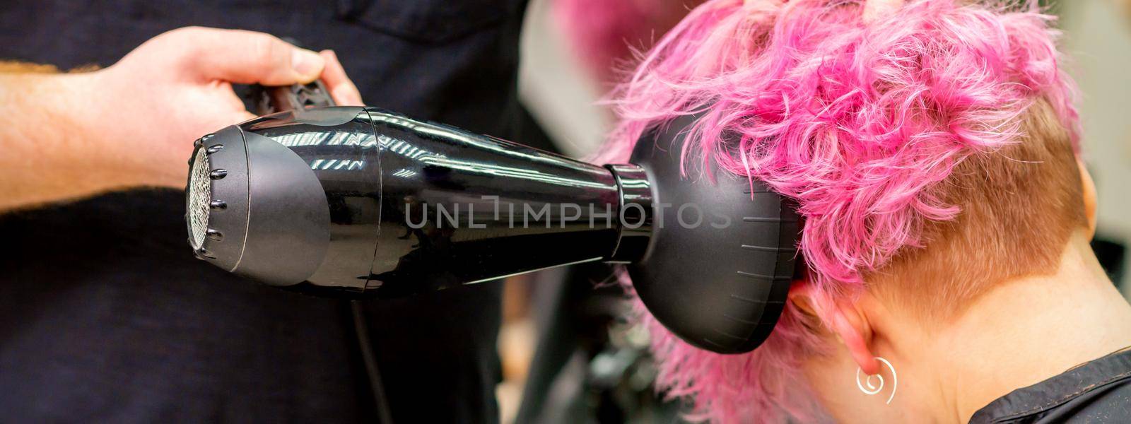 Close up of hairdresser drying short pink or red hair with a hairdryer in a beauty salon