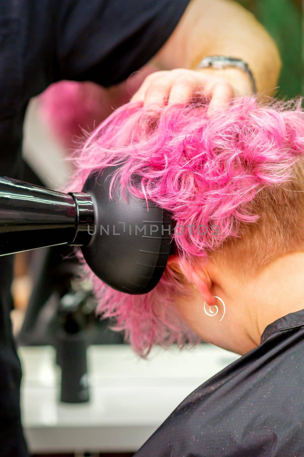 Close up of hairdresser drying short pink or red hair with a hairdryer in a beauty salon