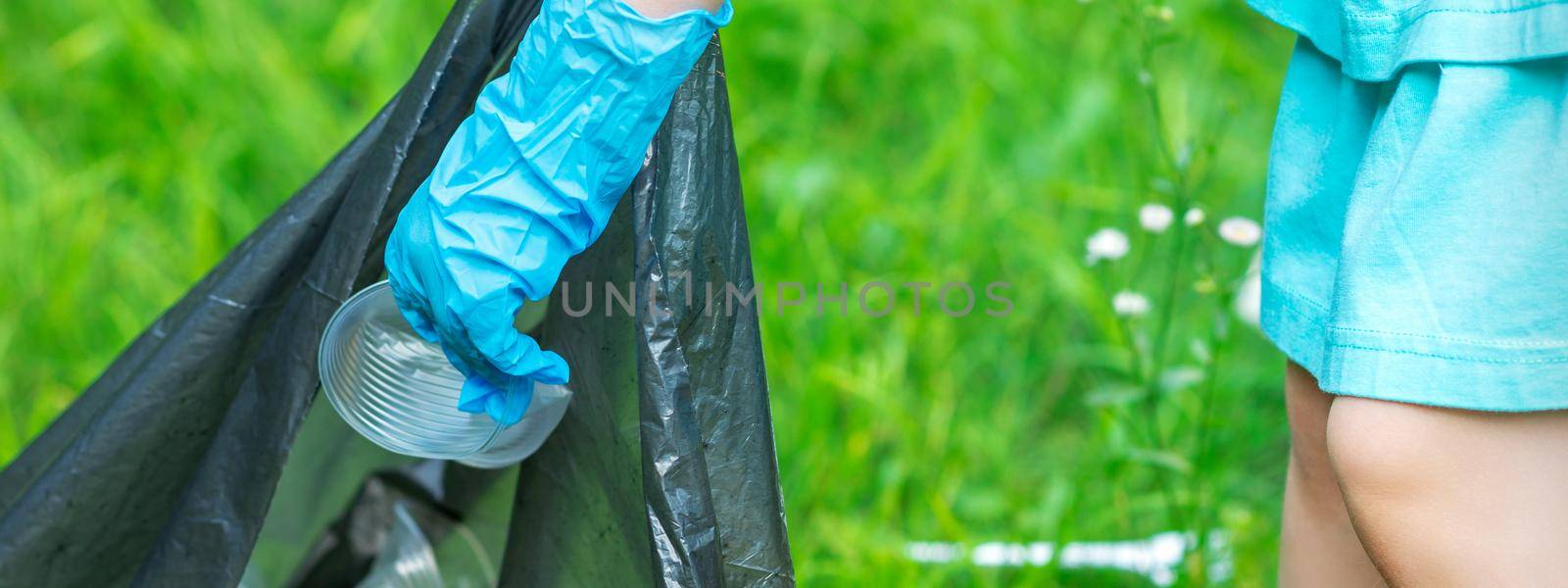 Child's hand puts plastic debris in the garbage bag in the park