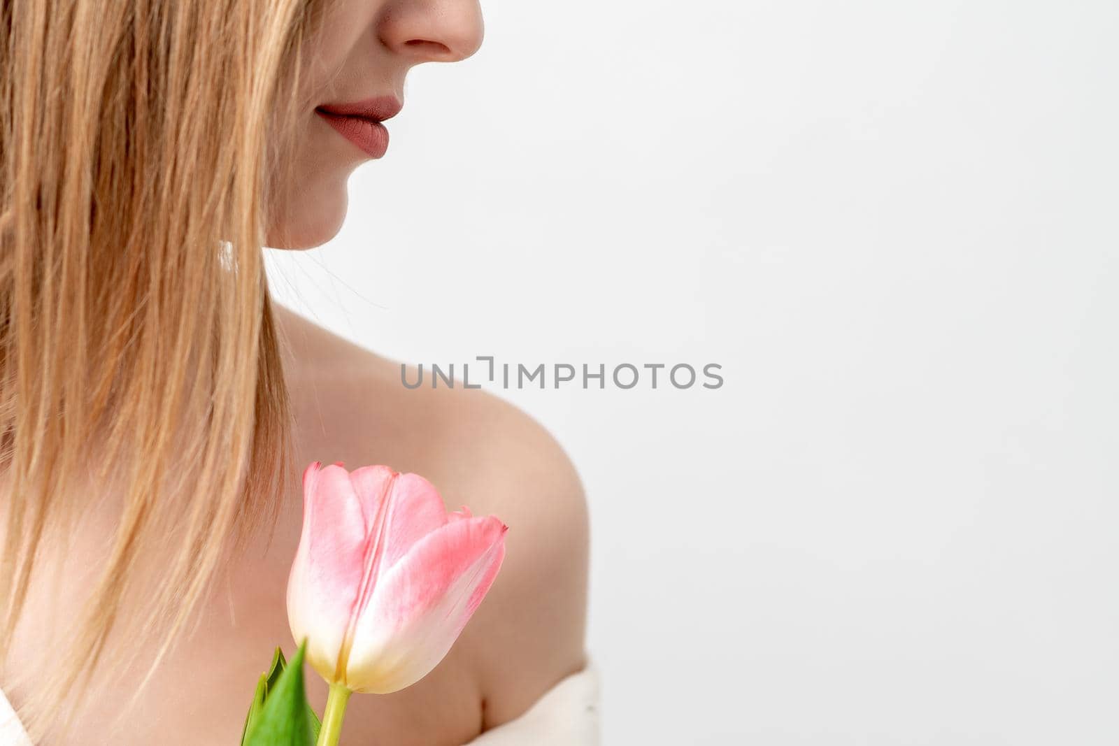 Half face portrait of a beautiful young caucasian woman with one pink tulip on white background