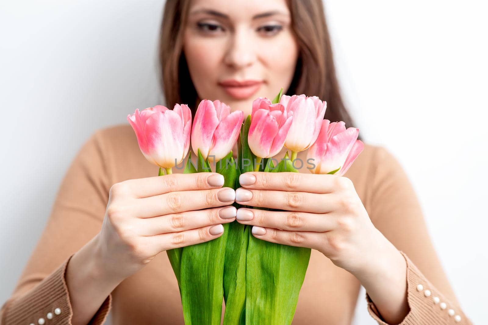 A young caucasian woman holds pink tulips in her hands against a white background