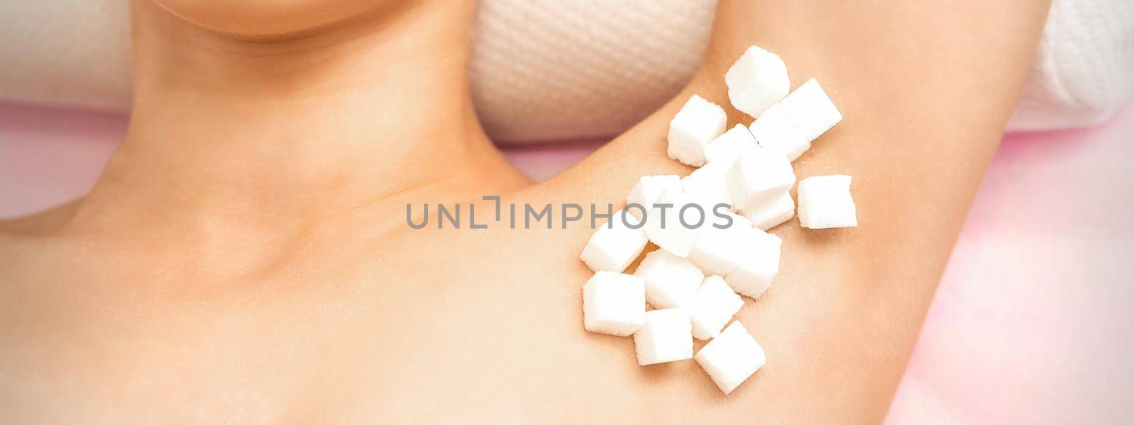 Sugaring concept. White sugar cubes lying on the armpit of a young female