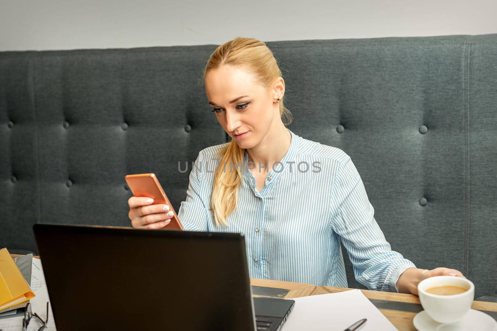 Young businesswoman using smartphone sitting at the table with laptop in cafe