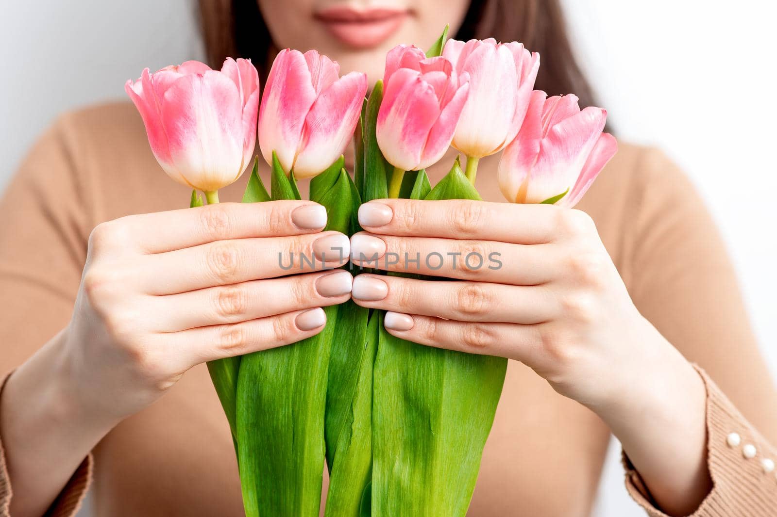 A young caucasian woman holds pink tulips in her hands against a white background