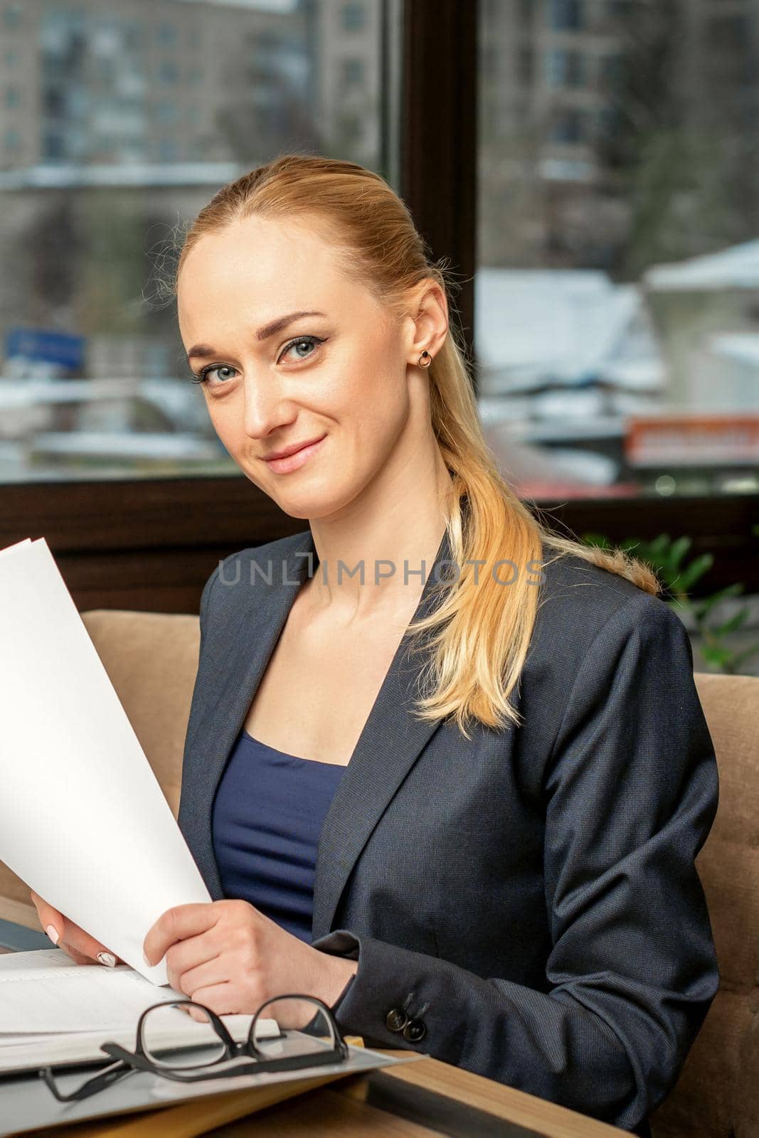 Portrait of a young smiling caucasian businesswoman prepares documents at the table looking at the camera in cafe
