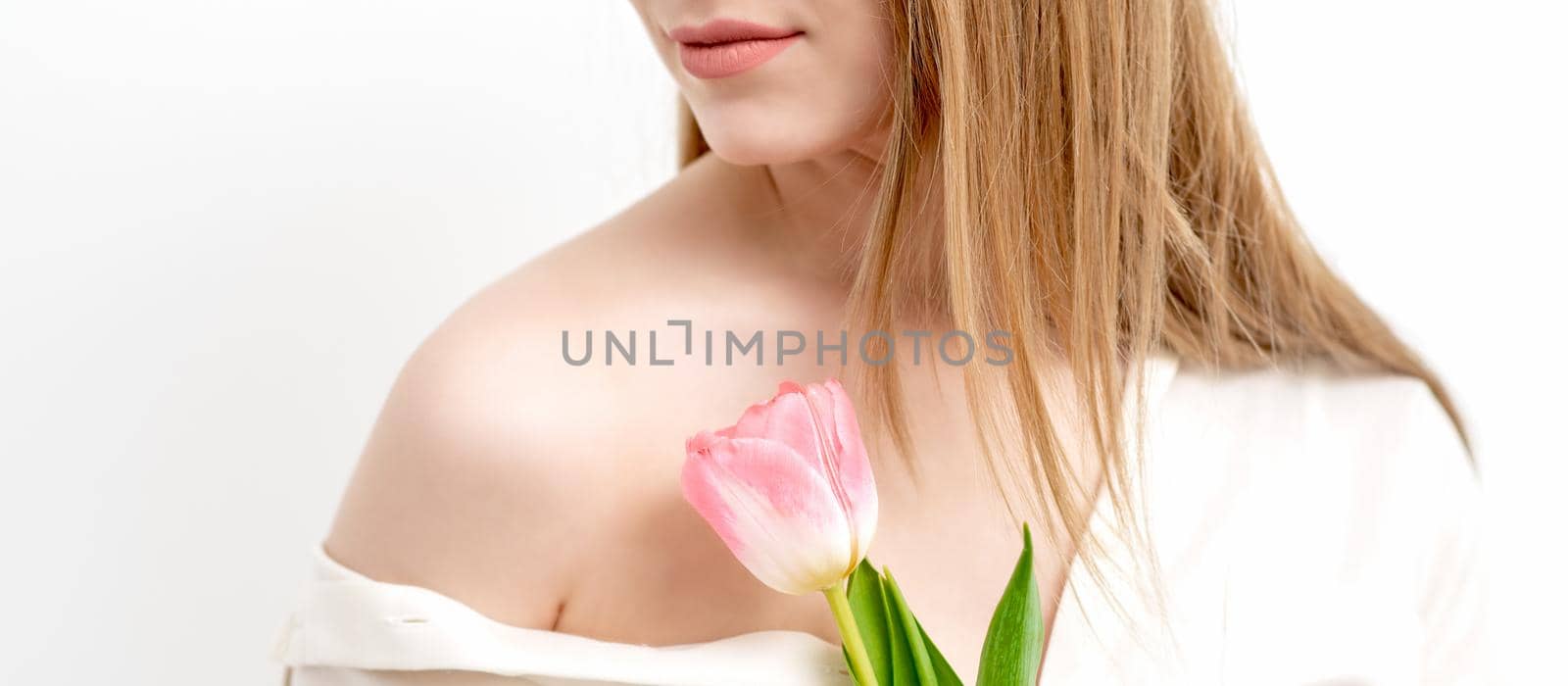 Half face portrait of a beautiful young caucasian woman with one pink tulip on white background
