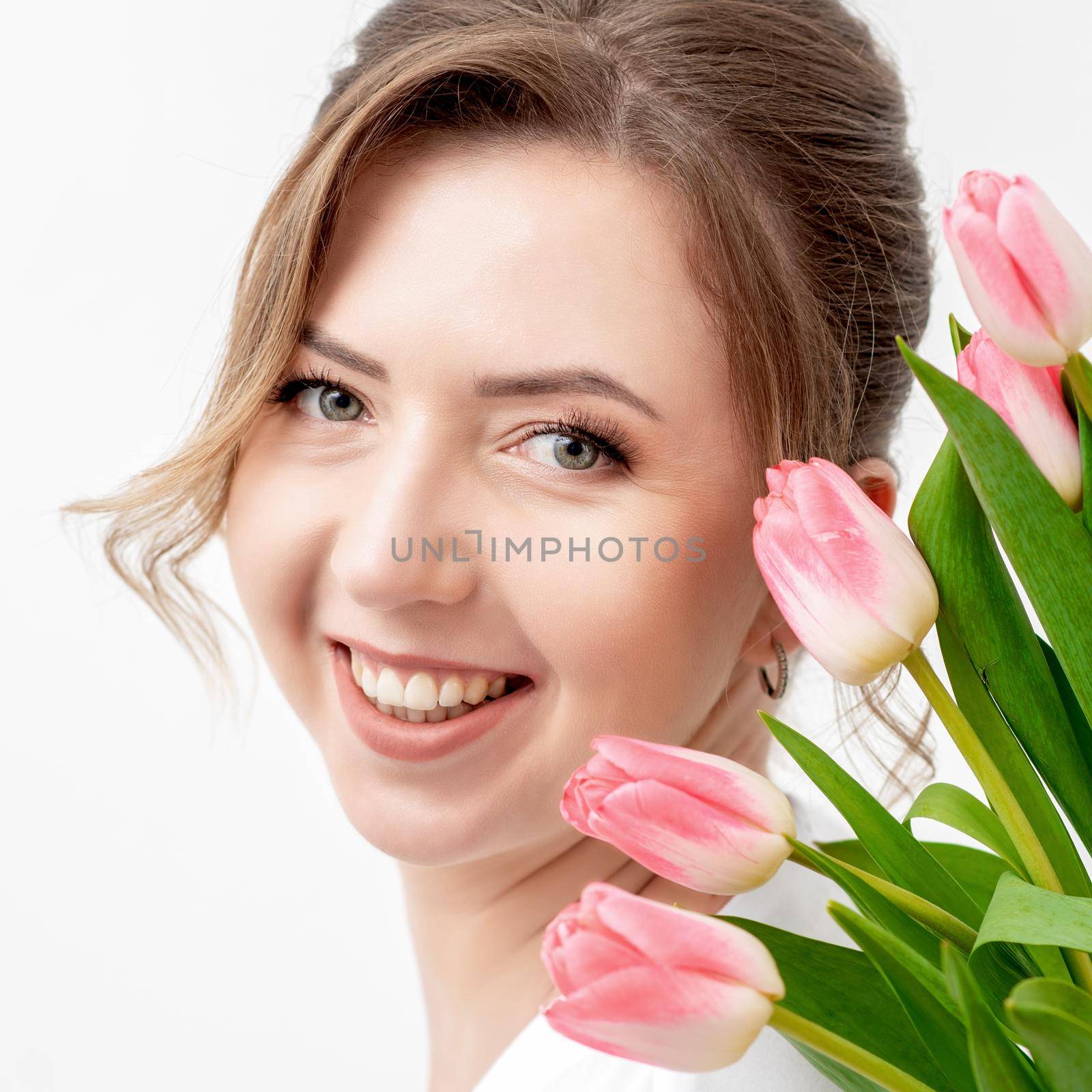 Portrait of a happy young caucasian woman with pink tulips against a white background