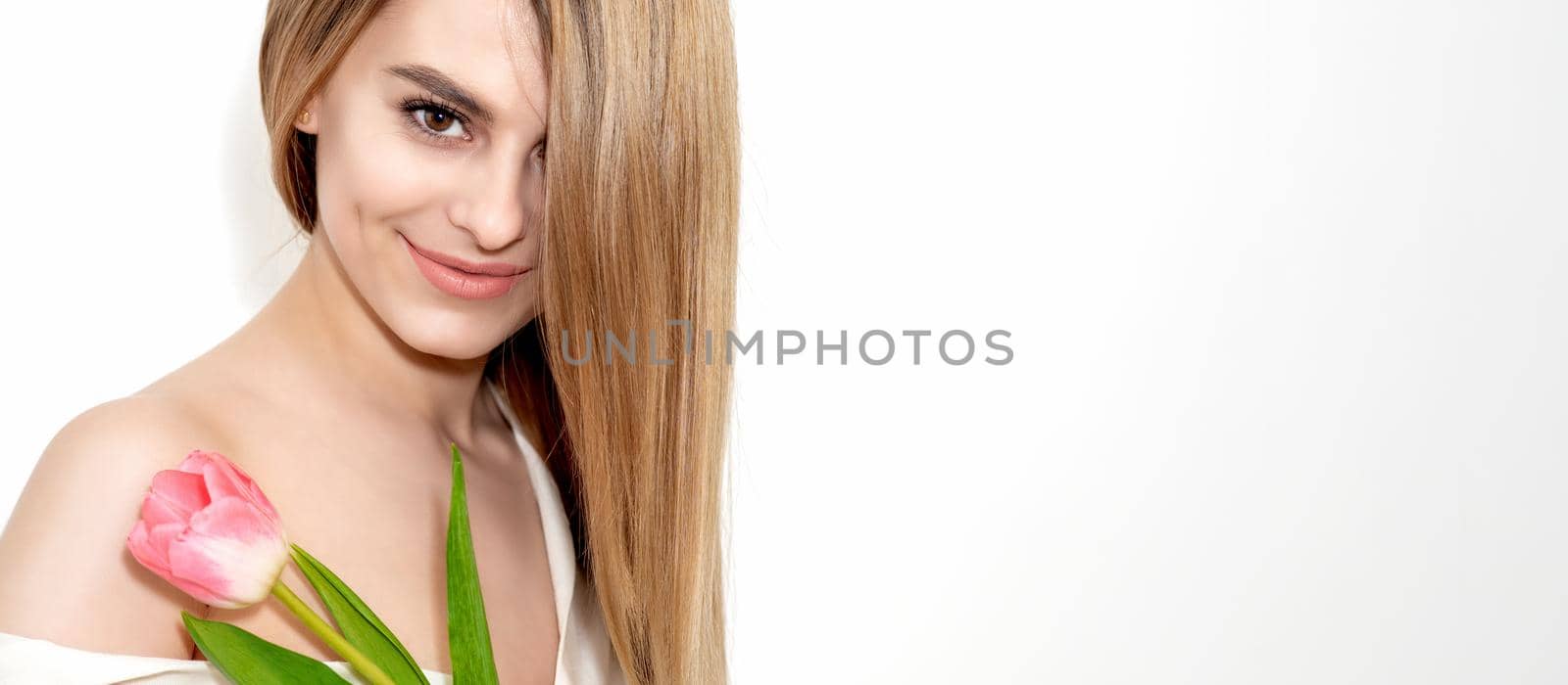 Portrait of a happy young caucasian woman with one pink tulip against a white background with copy space