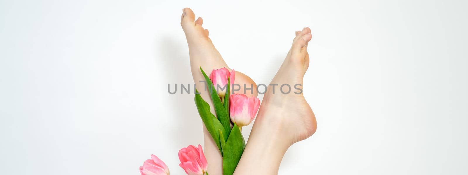 Beautiful slim smooth woman's legs with tulips flowers on white background