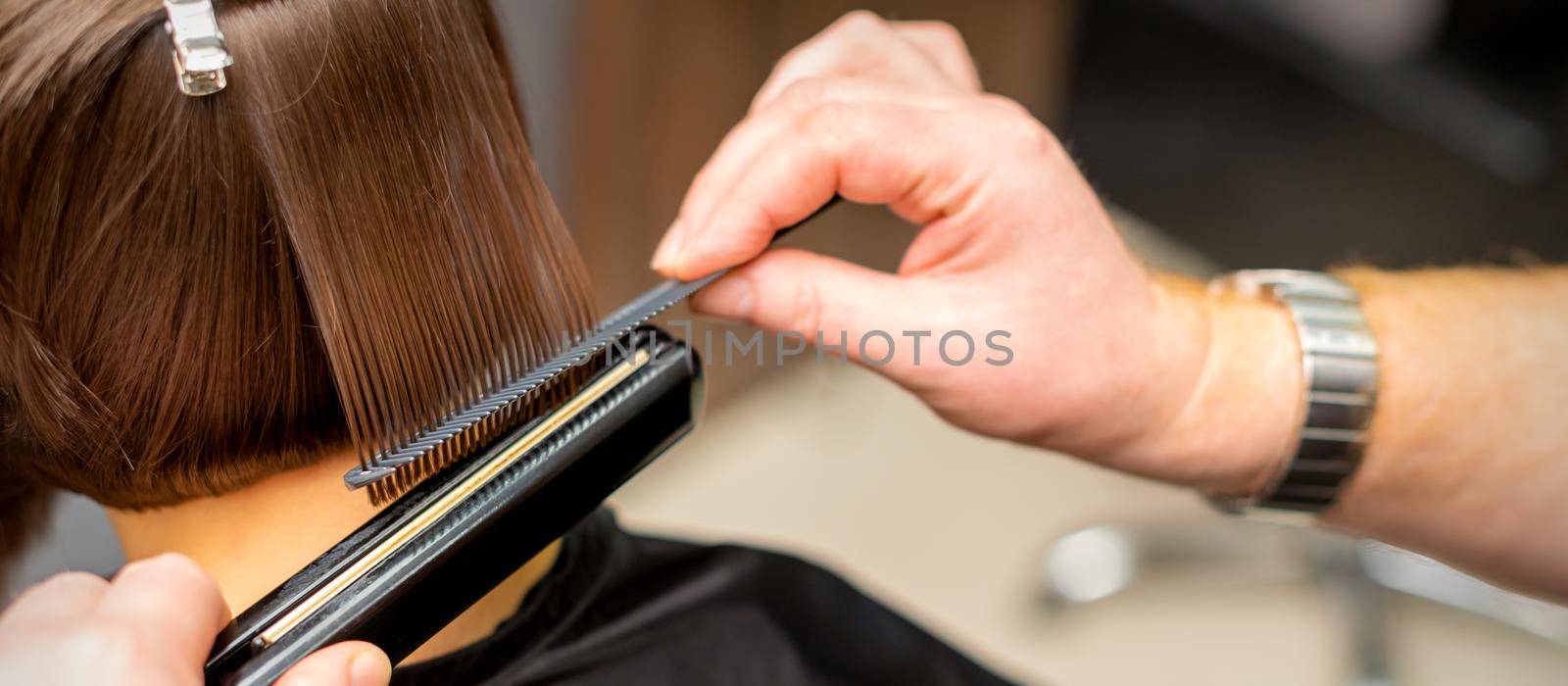 Close up of the hairdresser straightening the short hair of a female client with a hair straightening iron in a beauty salon