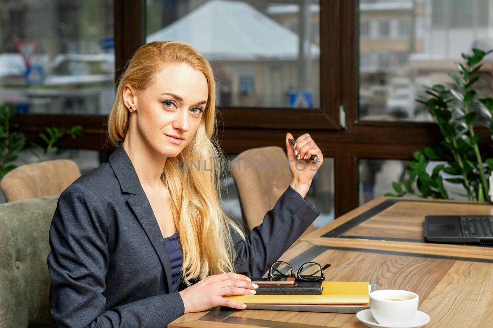 Portrait of a young caucasian businesswoman with documents and laptop at the table looking at the camera in cafe